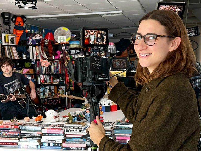 Maia Stern looks over her shoulder and smiles from behind a video camera filming a band playing.